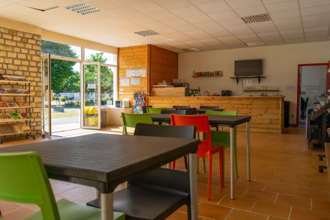Espace café lumineux à Onlycamp Camping La Gâtine, Centre-Val de Loire, avec chaises colorées et grande baie vitrée.
