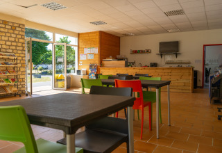 Espace café lumineux à Onlycamp Camping La Gâtine, Centre-Val de Loire, avec chaises colorées et grande baie vitrée.