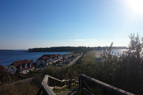 Uitzicht vanaf een trap bij Am Strand lodge in Duitsland met huizen, strand en zee onder blauwe lucht.