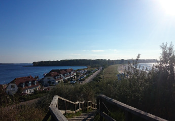 View from stairs at Am Strand lodge in Germany showing houses, a beach, parking, and the blue sea.