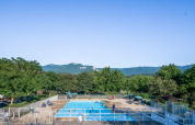 Buitenzwembad bij Onlycamp Camping Les Tuillères, omgeven door bomen en bergen in Auvergne-Rhône-Alpes.