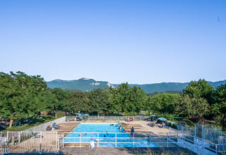 Buitenzwembad bij Onlycamp Camping Les Tuillères, omgeven door bomen en bergen in Auvergne-Rhône-Alpes.
