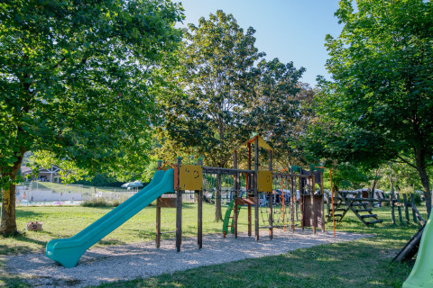 Speelplein met glijbaan en klimrek tussen groene bomen op Onlycamp Camping Les Tuillères in Frankrijk.