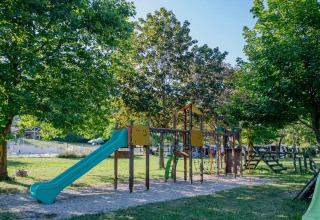 Spielplatz mit Rutsche und Klettergerüst unter grünen Bäumen auf Onlycamp Camping Les Tuillères in Frankreich.