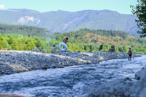 Mensen genieten bij een rivier met bergen bij Onlycamp Camping Les Tuillères in Auvergne-Rhône-Alpes, Frankrijk.