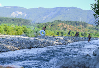 Folk nyder en flod og bjerge ved Onlycamp Camping Les Tuillères i Auvergne-Rhône-Alpes, Frankrig.