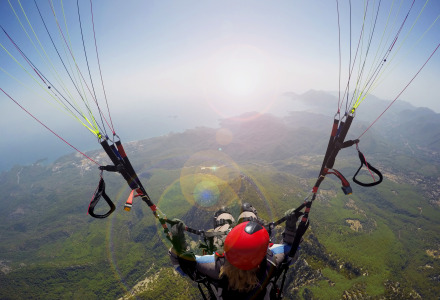 Gleitschirmflieger schwebt hoch über einer grünen Landschaft mit Blick auf Hügel und das Meer am Horizont.