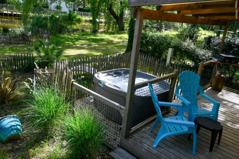 Deck esterno presso Zen Mobile Home con vasca idromassaggio, sedie blu, verde e vista su uno stagno.
