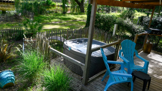 Outdoor deck at Zen Mobile Home featuring a hot tub, two blue chairs, lush greenery, and a small pond.