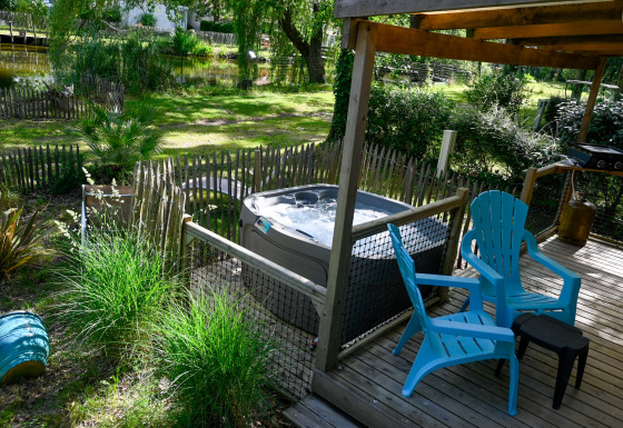 Deck esterno presso Zen Mobile Home con vasca idromassaggio, sedie blu, verde e vista su uno stagno.
