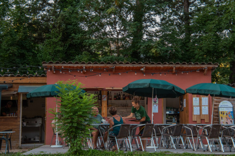 Outdoor café at Onlycamp Camping Chamarges in Auvergne-Rhône-Alpes, France, with guests and green umbrellas.
