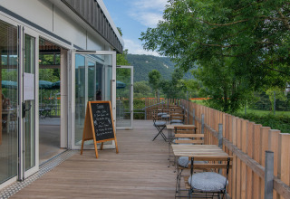 Udendørs terrasse med borde og stole med udsigt over grønne omgivelser på Onlycamp Camping de Besançon.