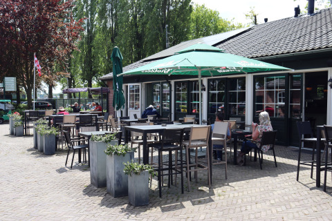 Outdoor lodge patio with tables, chairs, parasols, and guests enjoying a sunny day among green trees.