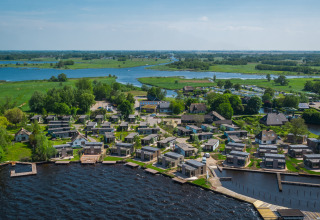 Aerial view of glamping accommodations by a lake, surrounded by fields and winding waterways.