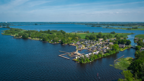 Vista aerea di un glamping sul lago con bungalow moderni, pontili in legno e vegetazione rigogliosa.