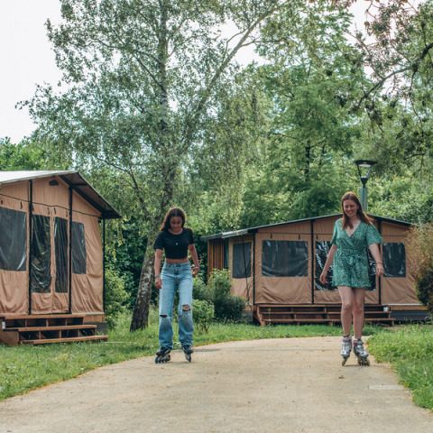 Zwei junge Frauen fahren Rollschuh vor Tiny Houses im Onlycamp Camping de Besançon in Frankreich.