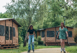 Zwei junge Frauen fahren Rollschuh vor Tiny Houses im Onlycamp Camping de Besançon in Frankreich.