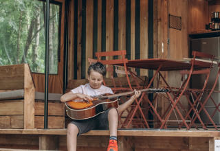 Junge spielt Gitarre auf der Terrasse des Chalet Galli Tiny House bei Onlycamp Camping de Besançon, Frankreich.