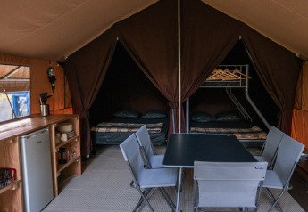 Vue intérieure de la tente safari Ponza à Onlycamp Camping de Besançon, avec coin repas et lits.