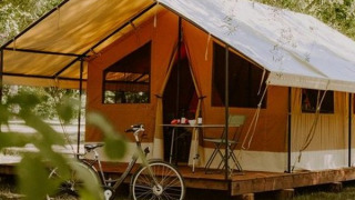 Tienda safari Ponza sobre plataforma de madera, bicicleta delante, rodeada de árboles y naturaleza verde.