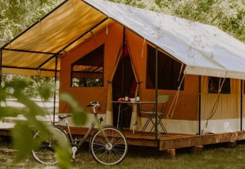 Tente safari Ponza sur terrasse en bois, vélo devant, entourée de verdure et d’arbres en été.