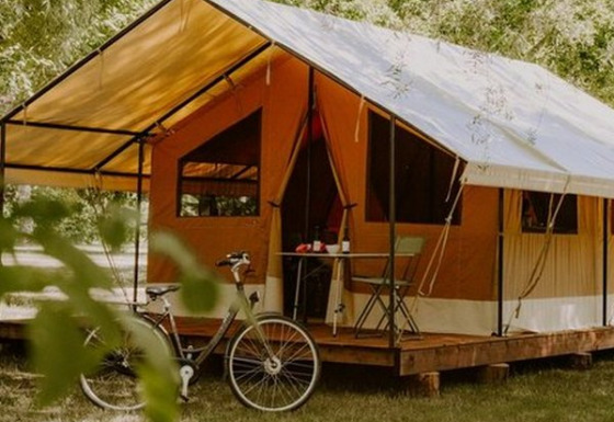 Tienda safari Ponza sobre plataforma de madera, bicicleta delante, rodeada de árboles y naturaleza verde.