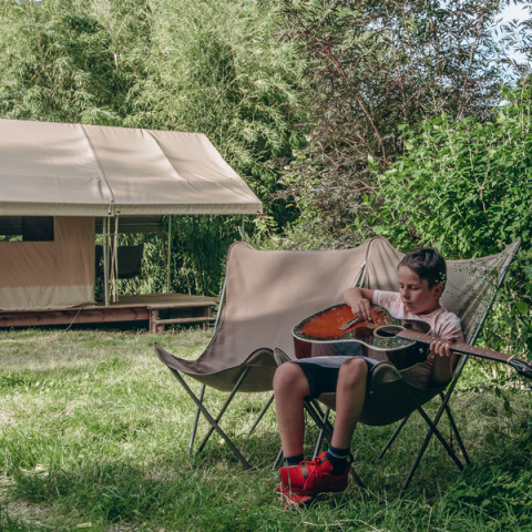 Dreng spiller guitar foran en Ponza safari-telt på Onlycamp Camping de Besançon i Frankrig.