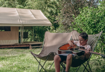 Junge spielt Gitarre neben einem Ponza-Safari-Zelt auf dem Onlycamp Camping de Besançon in Frankreich.