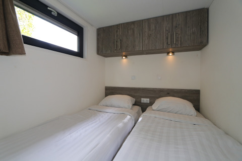 Slaapkamer met twee enkele bedden, houten kasten en verlichting in de Tiny Lodge te De Wije Werelt.