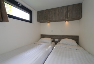 Slaapkamer met twee enkele bedden, houten kasten en verlichting in de Tiny Lodge te De Wije Werelt.
