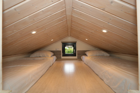 Slaapzolder in Tiny Lodge bij De Wije Werelt, Nederland, met twee eenpersoonsbedden en houten plafond.