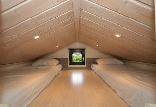 Slaapzolder in Tiny Lodge bij De Wije Werelt, Nederland, met twee eenpersoonsbedden en houten plafond.