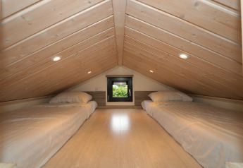Chambre en mezzanine au Tiny Lodge de De Wije Werelt, Pays-Bas, avec deux lits simples et plafond en bois.