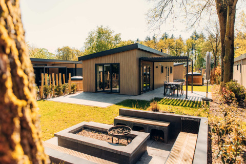 Modern Loevestein Deluxe lodge with hot tub, patio seating, and lush garden set amidst green trees.