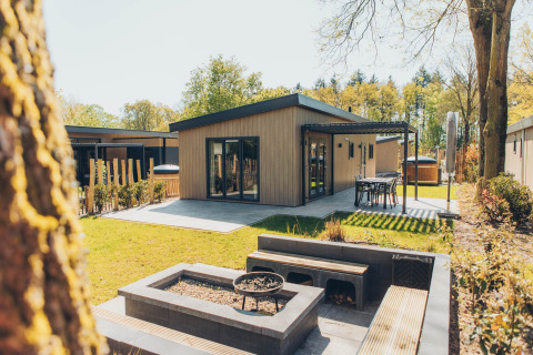 Lodge Loevestein Deluxe moderne avec bain à remous, terrasse, coin repas et jardin entouré d’arbres verts.