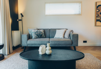 Sala moderna con sofá gris, cojines decorativos y mesa negra en Loevestein Deluxe, parque Veluwe.