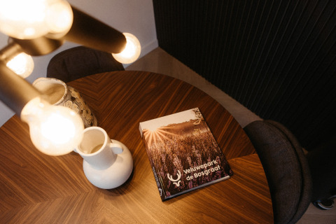 Table ronde en bois avec brochure de Veluwepark de Bosgraaf, carafe et lampe dans un lodge néerlandais.