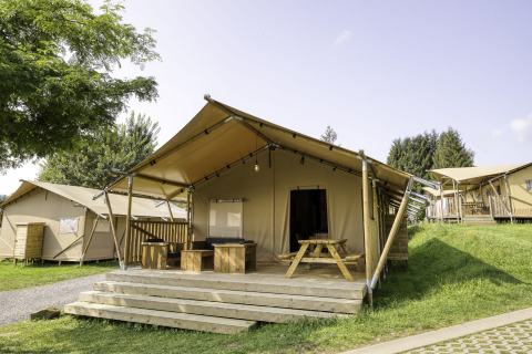 Safaritent Sunshine 49 met ruime veranda en houten meubels op een groene camping onder een heldere lucht.
