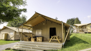 Tente safari Sunshine 49 avec grande terrasse et mobilier en bois sur un terrain de camping verdoyant.
