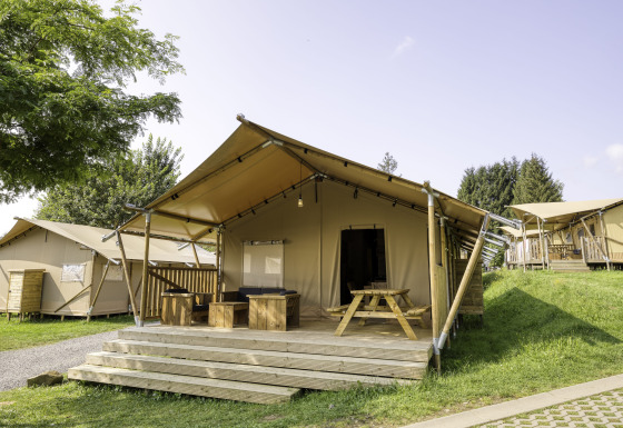 Safaritent Sunshine 49 met ruime veranda en houten meubels op een groene camping onder een heldere lucht.