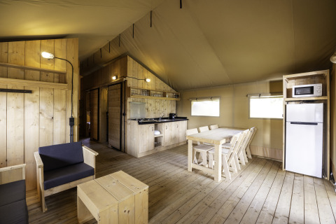 Interieur van safaritent 'Sunshine 49' bij Petite Suisse in België, met houten meubels en kitchenette.