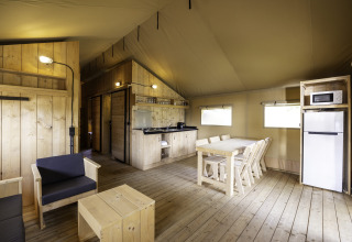 Interieur van safaritent 'Sunshine 49' bij Petite Suisse in België, met houten meubels en kitchenette.