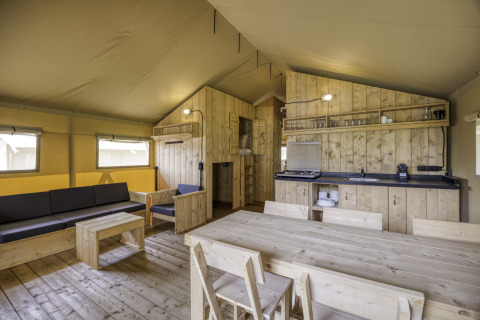Interieur van safaritent Sunshine 49 bij Petite Suisse in België met houten meubels en een keukenblok.