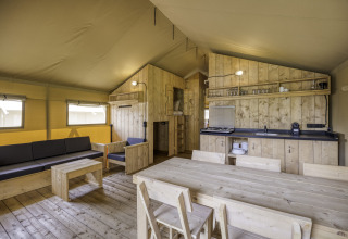 Interieur van safaritent Sunshine 49 bij Petite Suisse in België met houten meubels en een keukenblok.