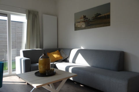 Moderne stue i Lodge 4, Breeduyn Village, Belgien, med grå sofaer, sofabord og stort vindue.