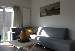Modernes Wohnzimmer in Lodge 4, Breeduyn Village, Belgien, mit grauem Sofa, Couchtisch und Wandbild.