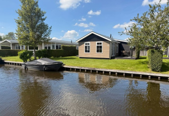 Cozy waterfront lodge with covered boat and green yard, photo taken at Stern 6 on a sunny day.