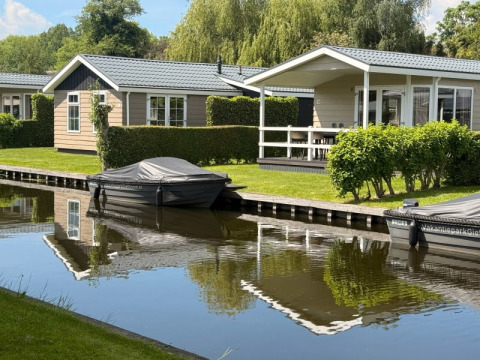 Moderne lodge Meerkoet 4 med både og kanaler, omgivet af grønne hække og træer i solskin.
