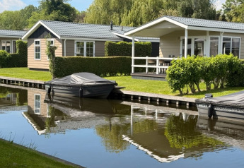 Lodge Meerkoet 4 moderne avec bateaux amarrés sur le canal, verdure et terrasse accueillante.
