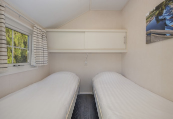 Deux lits simples et une fenêtre avec des rideaux rayés dans Tiny House 2 à Giethoorn, aux Pays-Bas.